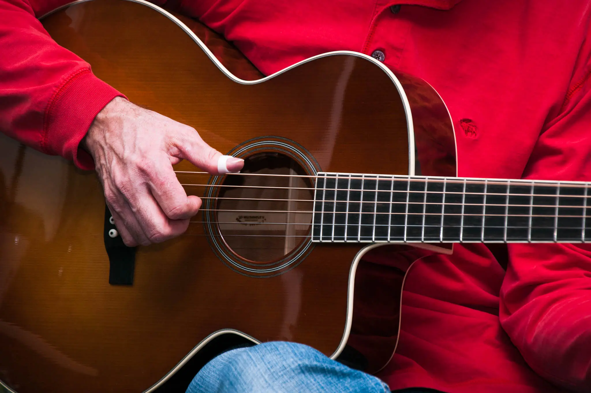 Close-up of a man playing an acoustic guitar with a cutaway and a sunburst top.