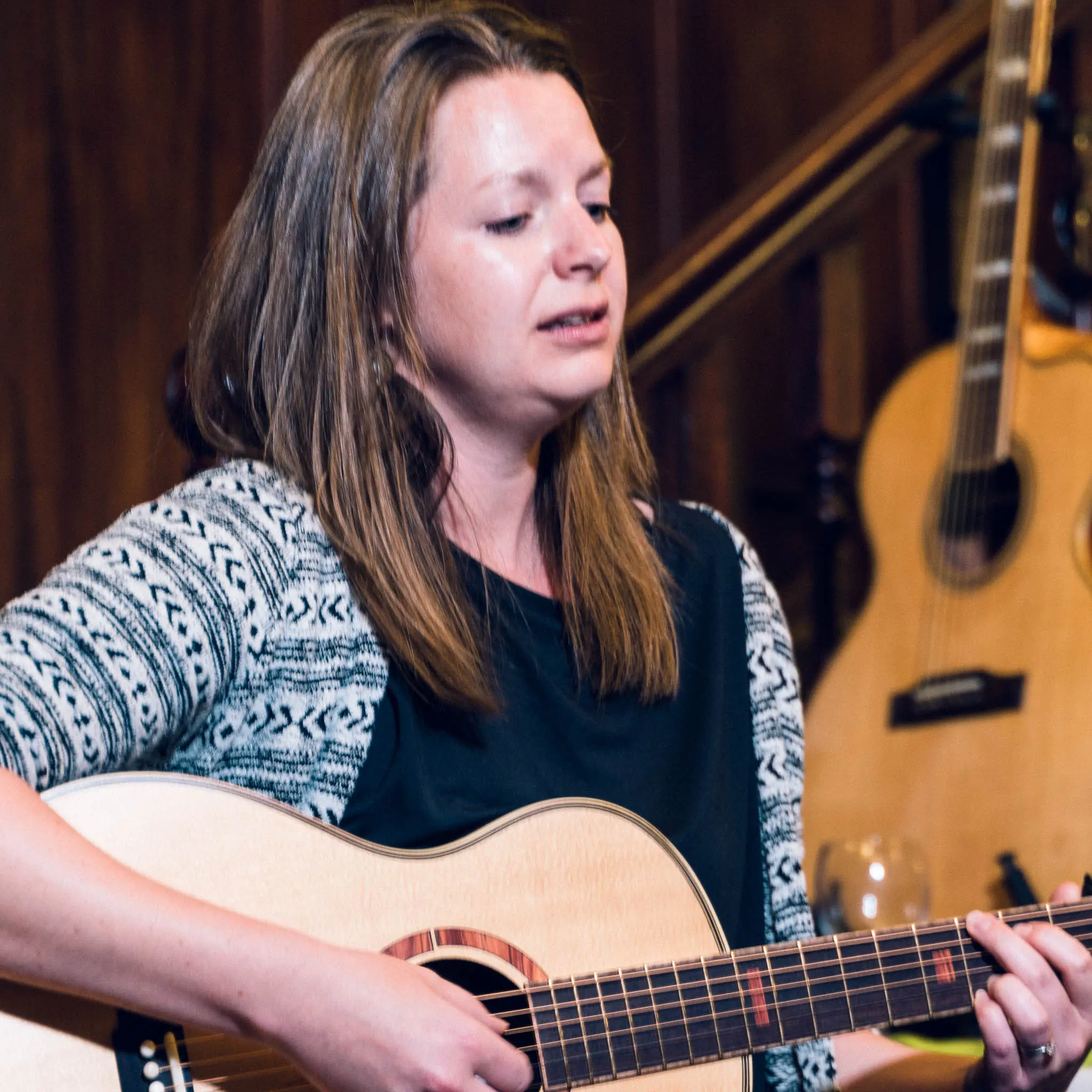 Square crop of Rosie Heydenrych playing acoustic guitar and singing